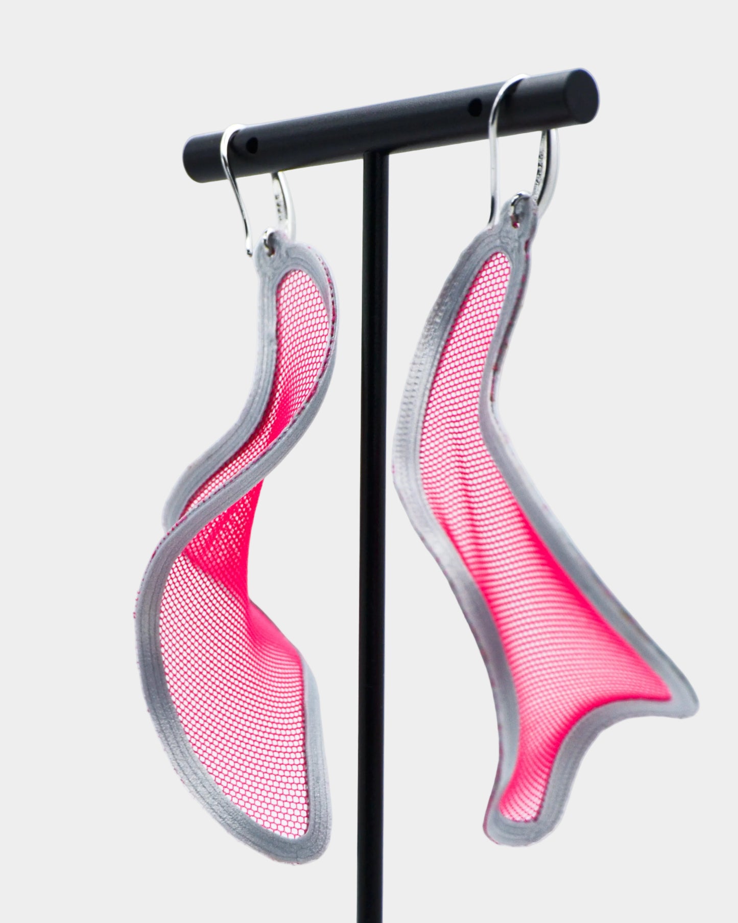 Pink and silver earrings on a stand against a white background