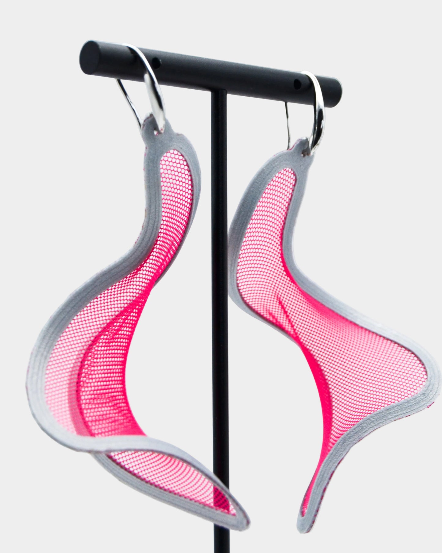 Pink and silver earrings on a stand against a white background