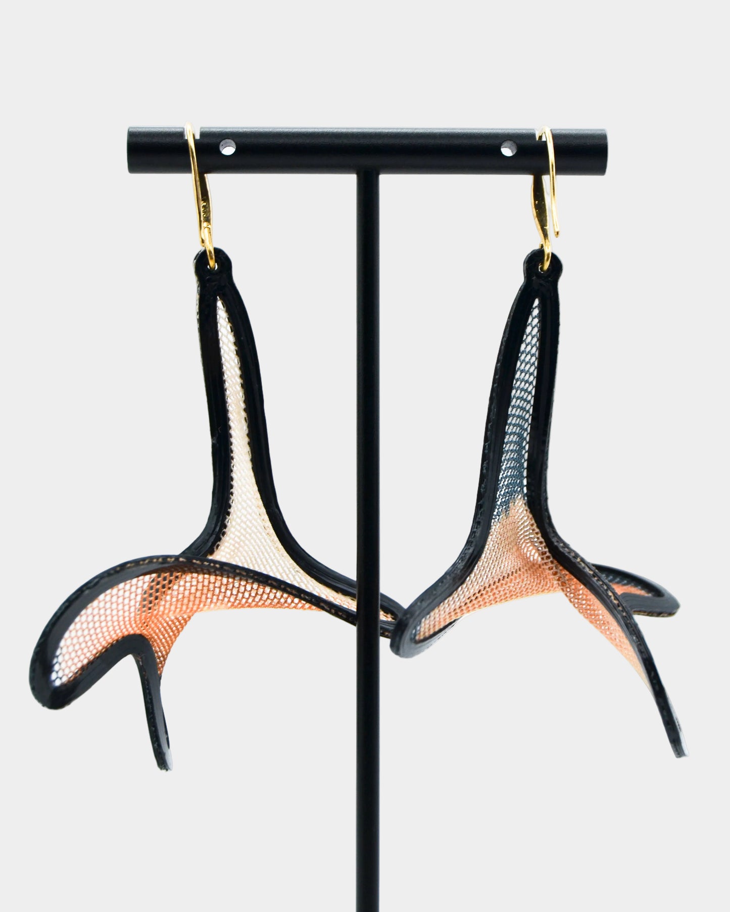 Pair of black and gold earrings on a black stand against a white background