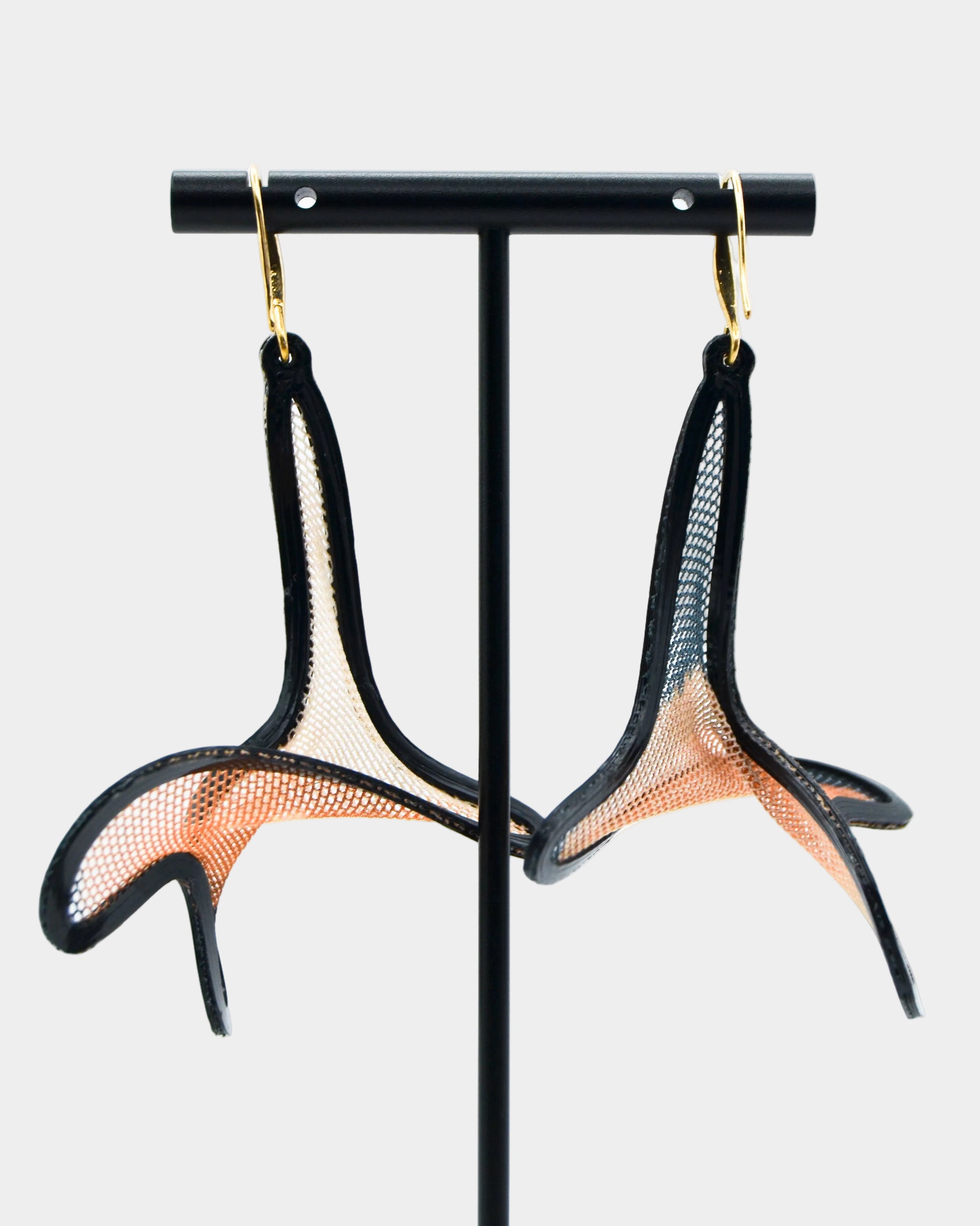 Pair of black and gold earrings on a black stand against a white background