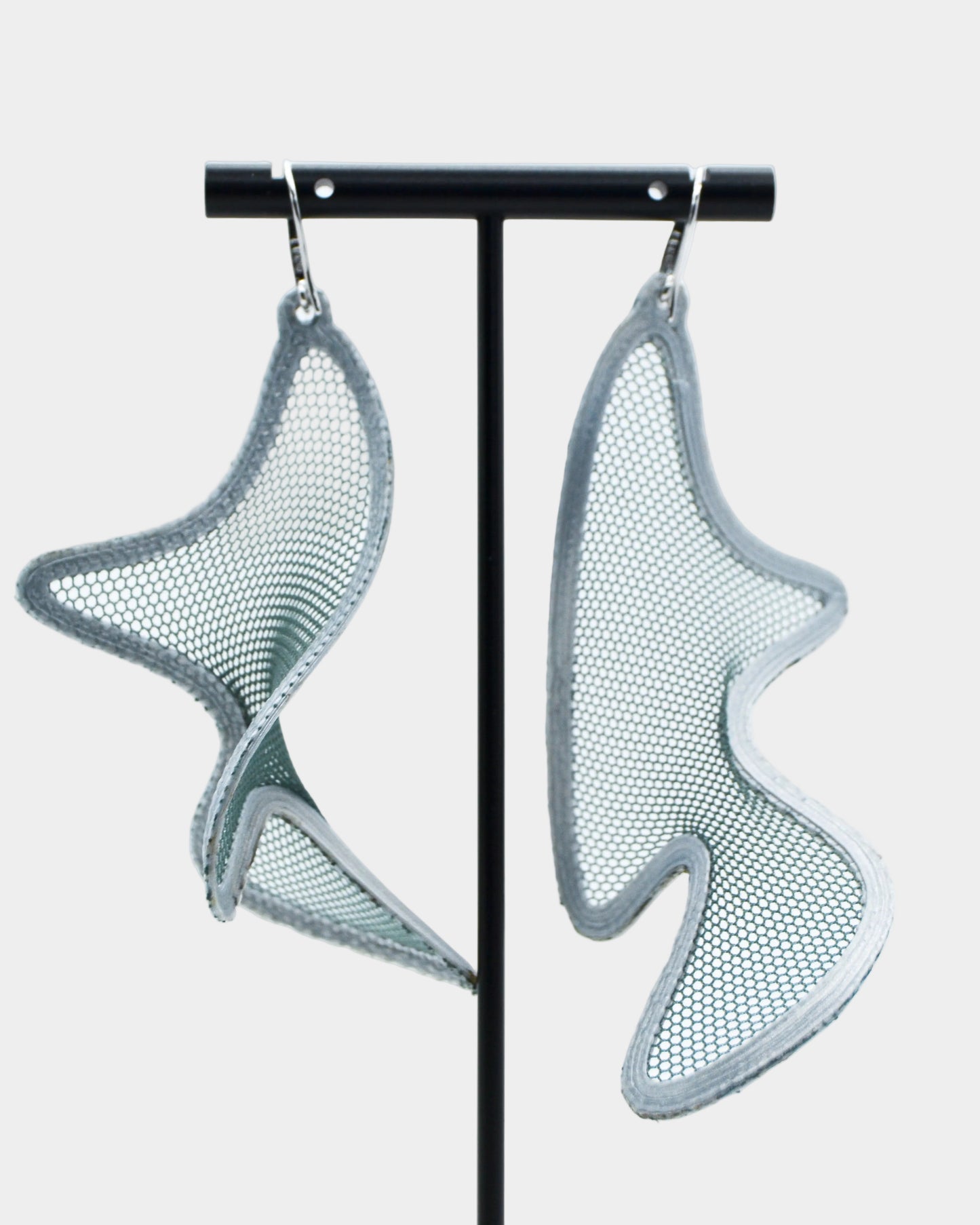 Pair of silver mesh earrings on a black stand against a white background