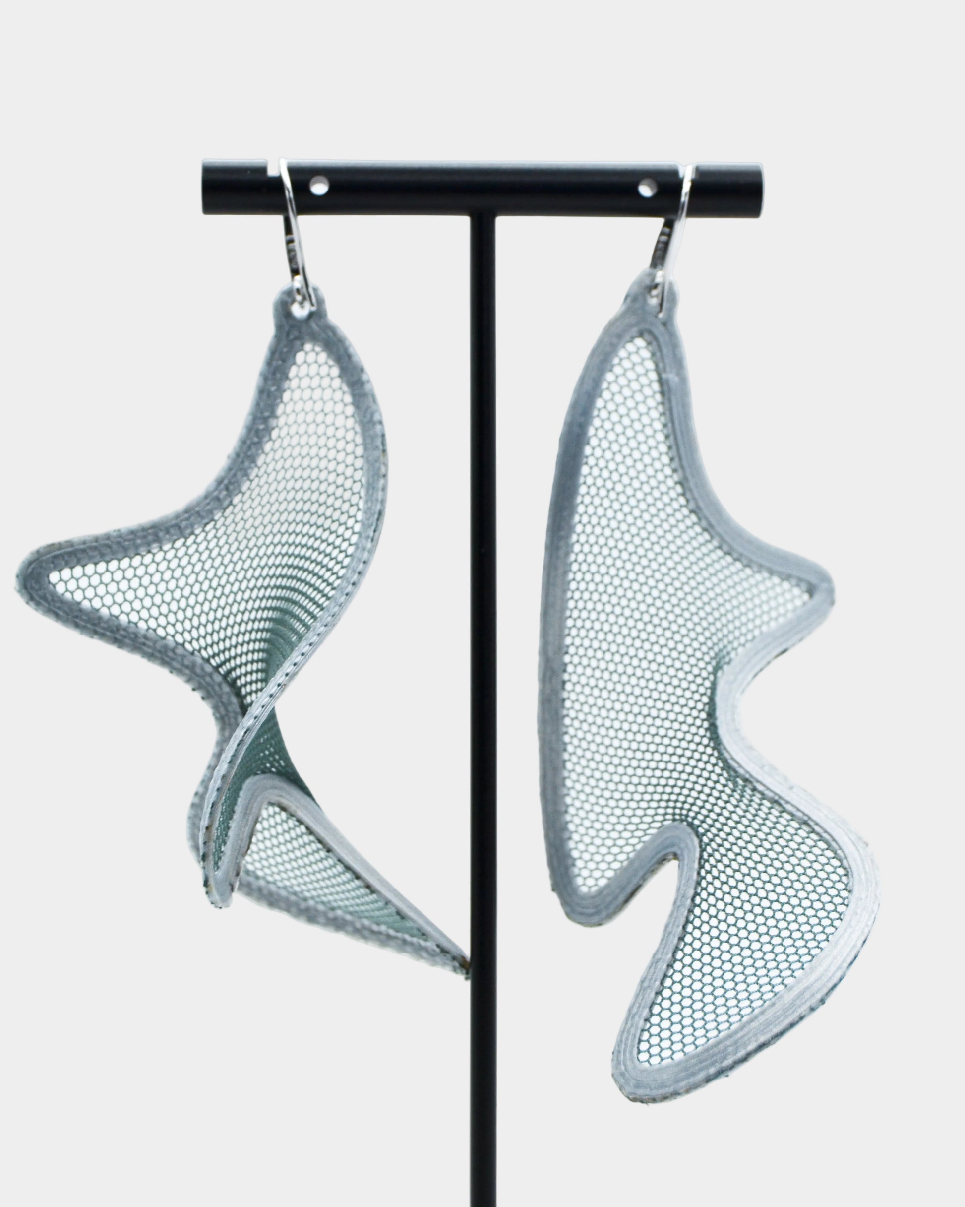 Pair of silver mesh earrings on a black stand against a white background