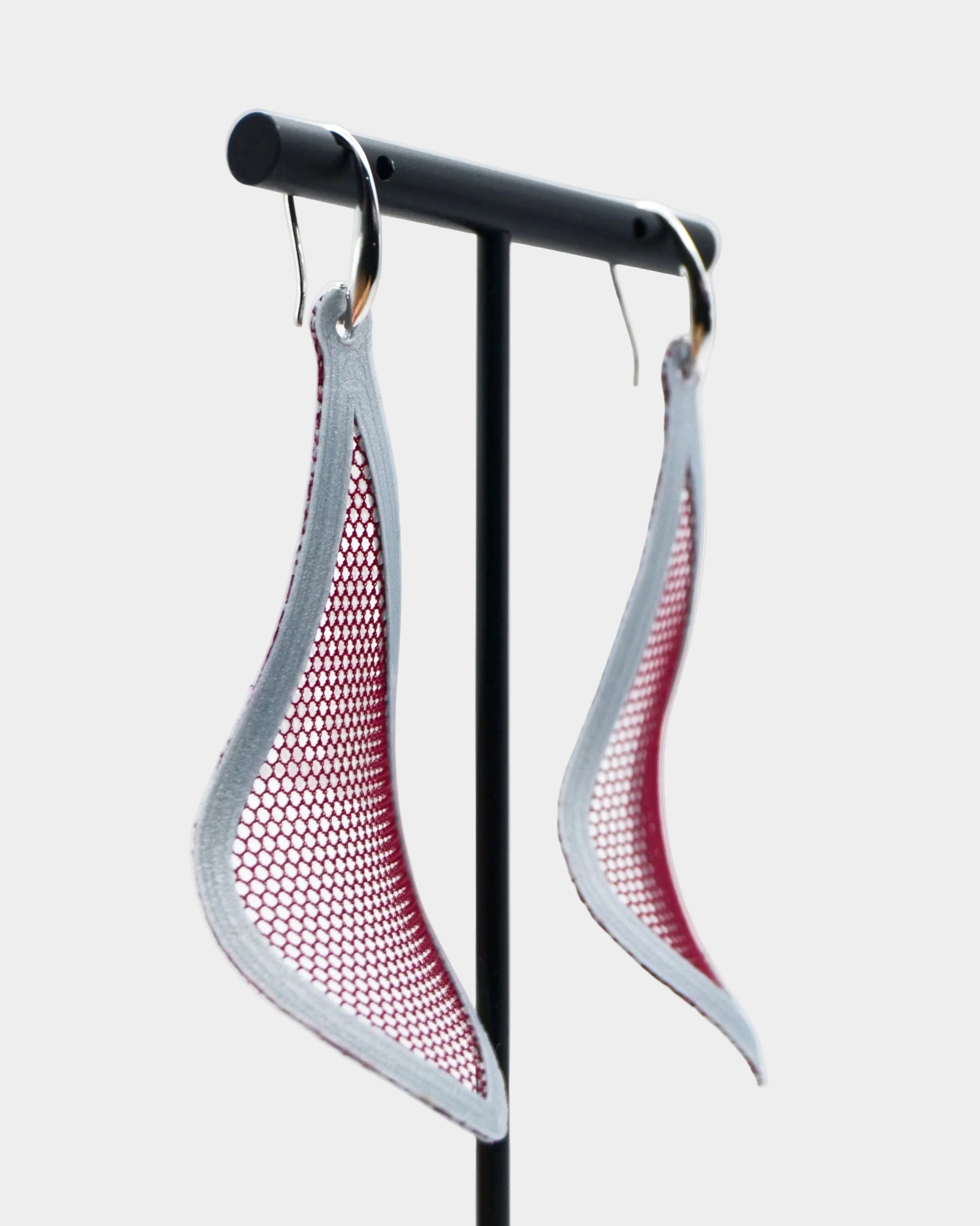 Pair of earrings with red and gray mesh design on a stand against a white background