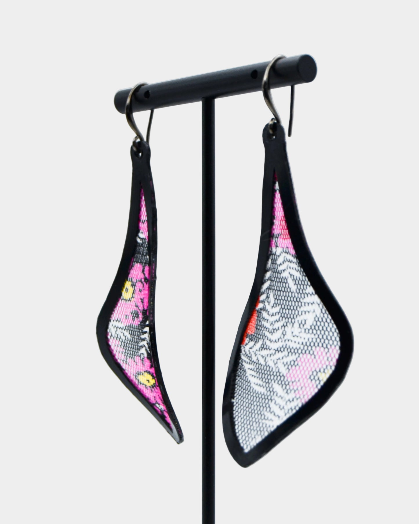 Pair of earrings on a stand with floral and geometric patterns against a light gray background